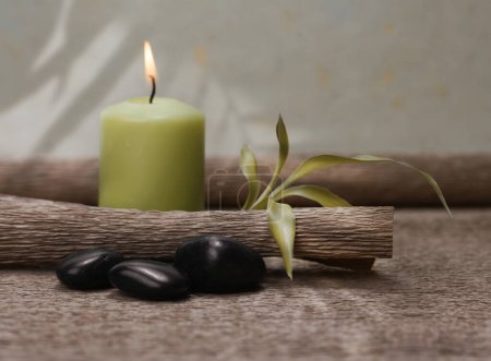 Téléchargez les photos : Bougie verte brûlante, pierres noires et feuille de bambou sur un tapis brun. Nature spa lumière et ombre fond. - en image libre de droit