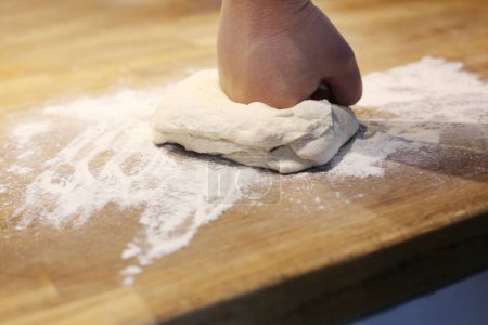 Photo for Maing homemade dough and kneeding it on a wooden kitchen worktop on a floured table - Royalty Free Image