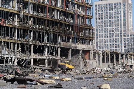 Foto de UCRANIA, KYIV, 25 DE MARZO DE 2022: Un misil ruso destruyó el centro comercial y de entretenimiento Retroville el 20 de marzo. Excavadora limpiando escombros. Después del bombardeo. Terror y genocidio del pueblo ucraniano - Imagen libre de derechos