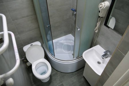 Téléchargez les photos : Intérieur de la salle de bains avec cuvette de toilette blanche, cabine de douche, lavabo, sèche-cheveux, porte-serviettes chauffant, miroir, armoire sous le lavabo et carreaux muraux et de sol gris - en image libre de droit
