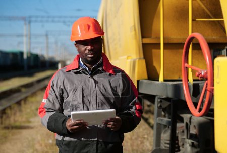 Photo for Inspector of wagons at freight train station with Tablet PC. African american railway man with tablet computer at freight train terminal - Royalty Free Image