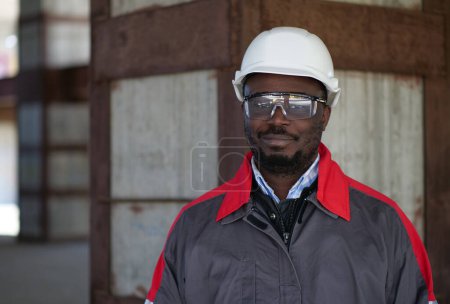 Téléchargez les photos : Un ouvrier afro-américain se tient sur le chantier, regarde la caméra et sourit - en image libre de droit