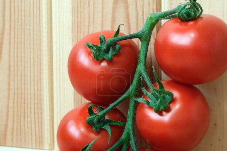 Vier reife Tomaten hängen an Haken an einer rustikalen Holzwand.