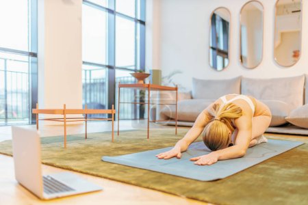 Téléchargez les photos : Femme utilisant un ordinateur portable pour pratiquer le yoga à la maison - en image libre de droit