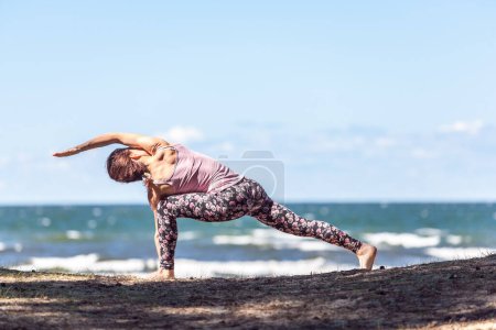 Téléchargez les photos : Jeune femme caucasienne pratiquant le yoga au bord de la mer, jour d'été - en image libre de droit