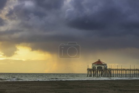 Photo for The storm clouds form over the Huntington Beach Pier and the sky ligts up at sunset - Royalty Free Image