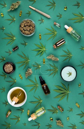 Foto de Composición laica plana con hojas de cáñamo y botellas de aceite esencial sobre fondo verde con espacio para el texto. - Imagen libre de derechos
