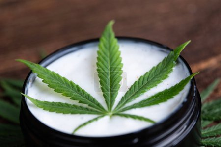Téléchargez les photos : Feuilles de chanvre de cannabis avec un pot en verre sur une planche en bois. - en image libre de droit