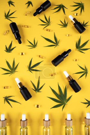 Foto de Aceite de cáñamo, botellas de aceite de cbd y cogollos de marihuana sobre fondo amarillo, puesta plana - Imagen libre de derechos