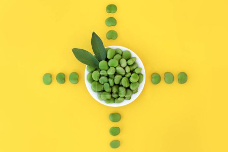Photo for Broad bean green vegetable nutritious health food, high in folate, fibre, antioxidants, potassium and vitamin b. Natural produce to lower cholesterol. Abstract design on yellow background. - Royalty Free Image
