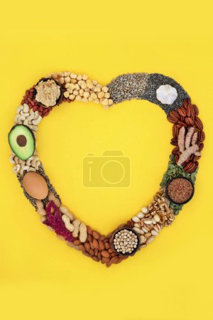 Photo for Heart shape wreath with essential fatty acids healthy heart food containing lipids unsaturated good fats for low cholesterol levels with nuts, seeds, vegetables, dairy, legumes and grain. On yellow. - Royalty Free Image