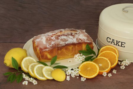 Lemon and orange lemon drizzle cake with fresh fruit, leaves, spring blossom and cake tin on rustic wood background. Homemade dessert for celebratory events.