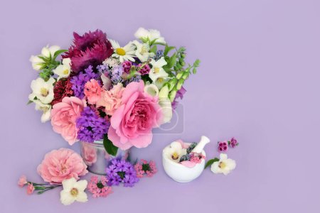 English summer flowers and herbs with mortar. Preparation of flora used in herbal medicine flower remedies on lilac background. Floral nature summertime composition.