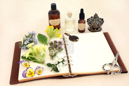 Naturopathic herbal medicine preparation with flowers, herbs and essential oil bottles with notebook. Natural spring floral nature concept for flower essences and remedies on hemp paper.