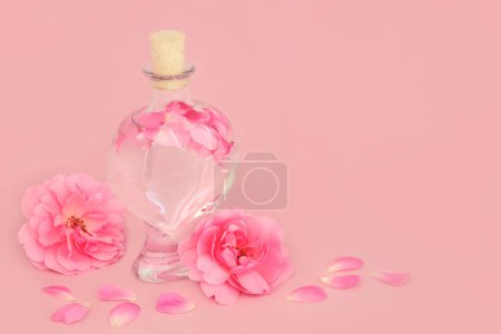 Photo for Rose flower perfume with flowers in heart shaped bottle with loose petals on pink. Natural floral beauty product, gift for Valentines Day, birthday, anniversary or Mothers day. - Royalty Free Image