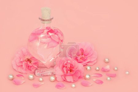 Photo for Rose flower perfume in heart shaped bottle with pearls, flowers and loose petals on pink. Natural beauty product, gift for Valentines Day, birthday, anniversary or Mothers day. - Royalty Free Image