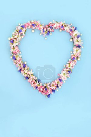 Photo for Heart shaped wreath with bluebell, apple blossom flowers and pearls for Spring and Beltane. Abstract floral design for birthday Mothers Day card, logo, gift tag or invitation on blue. - Royalty Free Image
