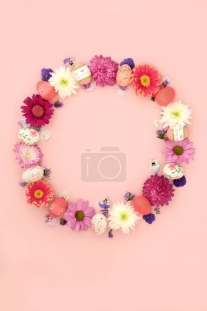 Easter wreath with flowers and decorated eggs on pink background. Decorative floral garland for traditional seasonal design.