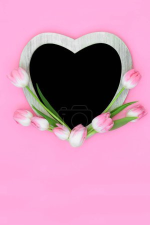 Foto de Forma de corazón rosa tulipán marco de flores con pizarra sobre fondo rosa.. Primavera floral mínima, Día de las Madres, Aniversario, cumpleaños y diseño de la naturaleza de Pascua. - Imagen libre de derechos