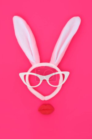 Easter bunny ears headband with pouting lips and glasses on vivid pink background. Abstract bizarre minimal  surreal face design for the holiday season.