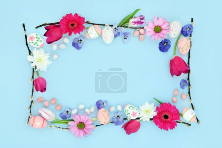 Happy Easter background border with edible and decorative eggs, flowers and willow branches on pastel blue. Flat lay. Natural nature frame design.