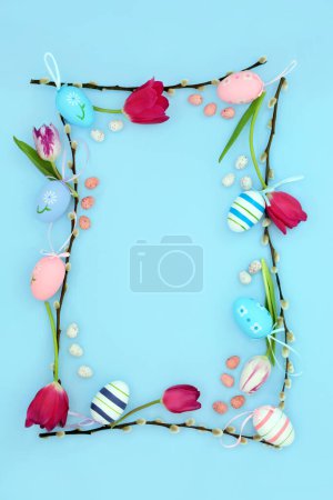 Easter background border with edible and decorative eggs, flowers and willow branch on pastel blue. Natural nature frame design for the holiday season. Flat lay.