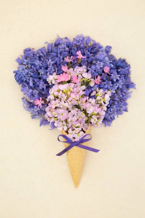 Surreal spring bluebell, red campion and nemesia flower ice cream cone on hemp paper background. Floral fun wildflower nature composition of springtime British flowers.