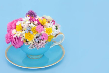 Flowers and wildflowers teacup surreal arrangement on blue background. Floral fun summer abstract food medicinal nature surrealism design.