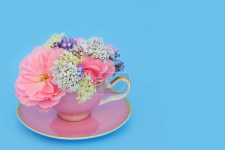Surreal rose, valerian, lavender and elder flowers in tea cup on blue. Fun food herbal medicine arrangement. Flowers have adaptogen relaxation tranquilizing health benefits.