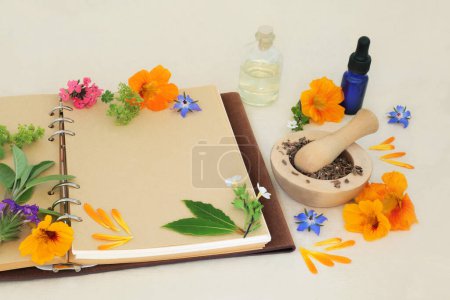 Flowers and herbs for naturopathic, medicinal and aromatherapy treatments. Herbal medicine ingredients for alternative remedies with recipe notebook on hemp paper background.