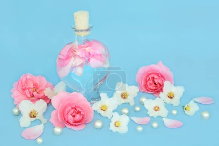 Rosewater for skincare with rose and orange blossom  flowers, heart shaped bottle and pearls on blue. Balances natural skin oils, reduce redness, naturally hydrates skin.