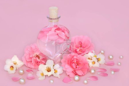 Rosen- und Orangenblütenduft in herzförmiger Flasche auf rosa mit lockeren Blüten und Perlen. Florales Schönheitsprodukt, Geschenk zum Valentinstag, Geburtstag, Jahrestag oder Muttertag.