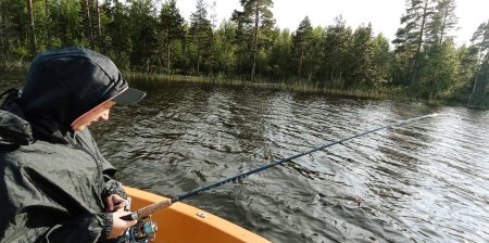 Téléchargez les photos : Jeune pêcheur pêche sur le bateau dans un lac suédois - en image libre de droit