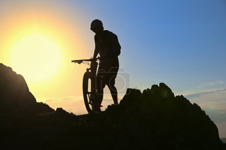 Téléchargez les photos : Silhouette d'un cycliste debout sur la falaise contre le soleil au printemps - en image libre de droit