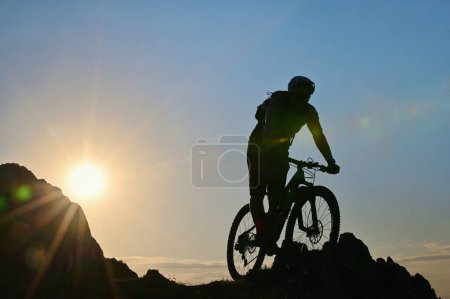 Photo for Silhouette Of A Cyclist Standing on Clif Against The Sun in Spring Time - Royalty Free Image