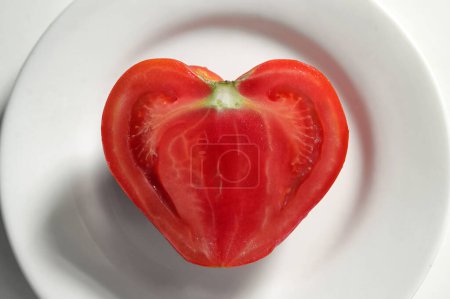 Téléchargez les photos : La moitié de la tomate fraîche en forme de coeur isolé sur plaque blanche - en image libre de droit