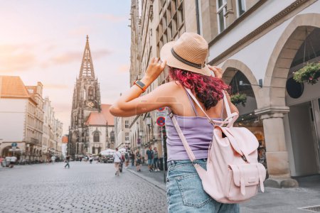 Foto de Mujer turista feliz con mochila visitando la calle Prinzipalmarkt y admirando edificios de arquitectura del casco antiguo en Munster, Alemania - Imagen libre de derechos
