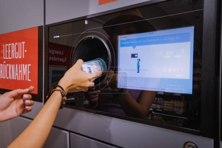 Téléchargez les photos : 25 juillet 2022, Munster, Allemagne : Une étudiante remet une bouteille de boisson en plastique pour recyclage à une machine automatisée. Style de vie respectueux de l'environnement et cashback - en image libre de droit