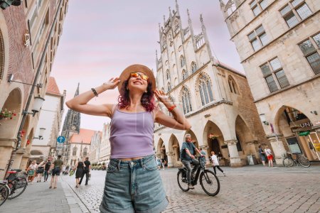 Foto de 25 Julio 2022, Munster, Alemania: Feliz turista visitando la calle Prinzipalmarkt y admirando edificios de arquitectura del casco antiguo - Imagen libre de derechos