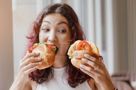 Glückliches Mädchen mit asiatischem und gemischtem Aussehen isst Hamburger oder Sandwich mit Appetit in einem Fast-Food-Café.