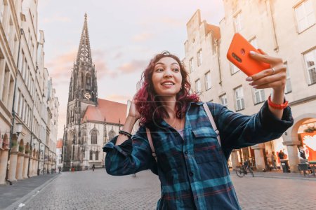 Foto de Chica turista feliz tomando foto selfie mientras visita la calle Prinzipalmarkt y admira los edificios de arquitectura del casco antiguo en Munster, Alemania - Imagen libre de derechos