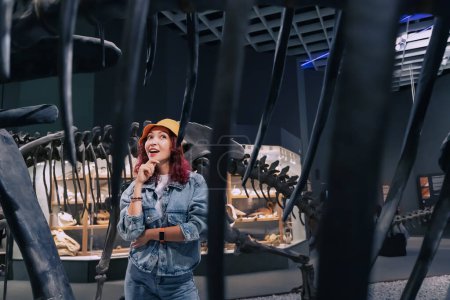 Foto de 26 de julio de 2022, Munster, Alemania: Muchacha turística emocionada en la excursión mira pensativamente los restos fosilizados de un esqueleto de dinosaurio en el Museo de Historia Natural. - Imagen libre de derechos