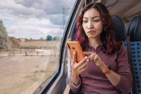 Fille agacée tente sans succès d'attraper un signal cellulaire ou une connexion Wi-Fi instable, tenant son smartphone dans ses mains dans le train