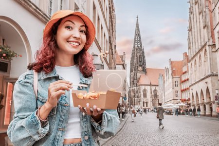 Foto de Alegre chica feliz merienda en comida rápida con camarones en masa en la calle de la ciudad de Munster en Alemania en una caja de papel para llevar - Imagen libre de derechos