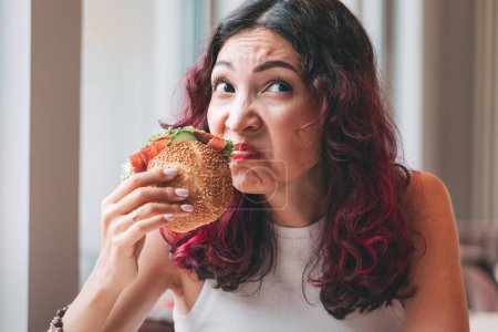 Una chica huele una hamburguesa estropeada. Alimentación rápida dieta y concepto de intoxicación alimentaria