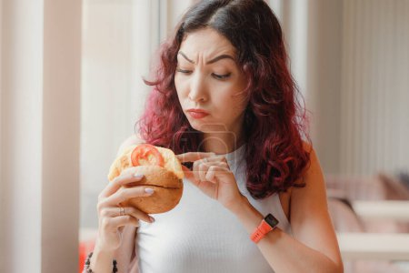 Téléchargez les photos : Une cliente mécontente d'un fast-food creuse dans un hamburger et trouve un produit gâté dans son déjeuner - en image libre de droit