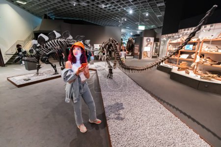 Foto de 26 de julio de 2022, Museo de Historia Natural de Munster, Alemania: Visitante con guía de aplicaciones para teléfonos inteligentes en la Exposición de aterradores esqueletos de dinosaurios - Imagen libre de derechos