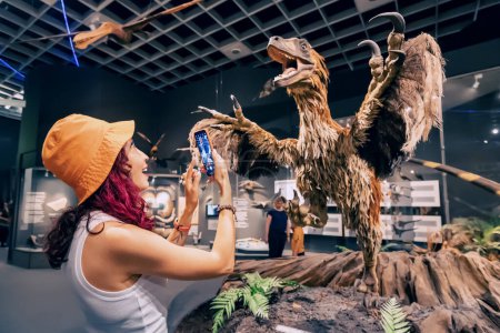 Foto de 26 de julio de 2022, Museo de Historia Natural de Munster, Alemania: Visitante con guía de aplicaciones para teléfonos inteligentes tomando fotos en la Exposición de aterradores dinosaurios emplumados - Imagen libre de derechos