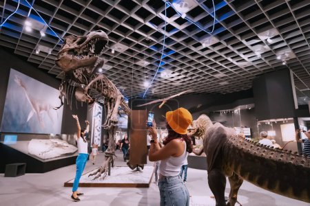 Foto de 26 de julio de 2022, Munster Natural History Museum, Alemania: Visitante con smartphone tomando fotos en la Exposición de terroríficos esqueletos de dinosaurios - Imagen libre de derechos