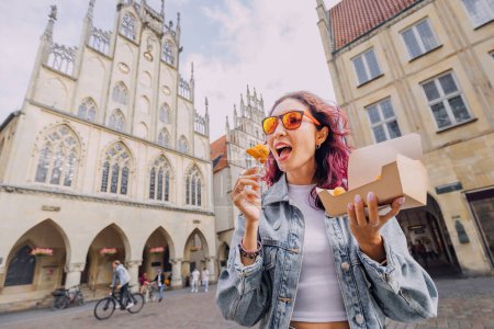 Foto de Alegre chica feliz merienda en comida rápida con camarones en masa en la calle de la ciudad de Munster en Alemania en una caja de papel para llevar - Imagen libre de derechos